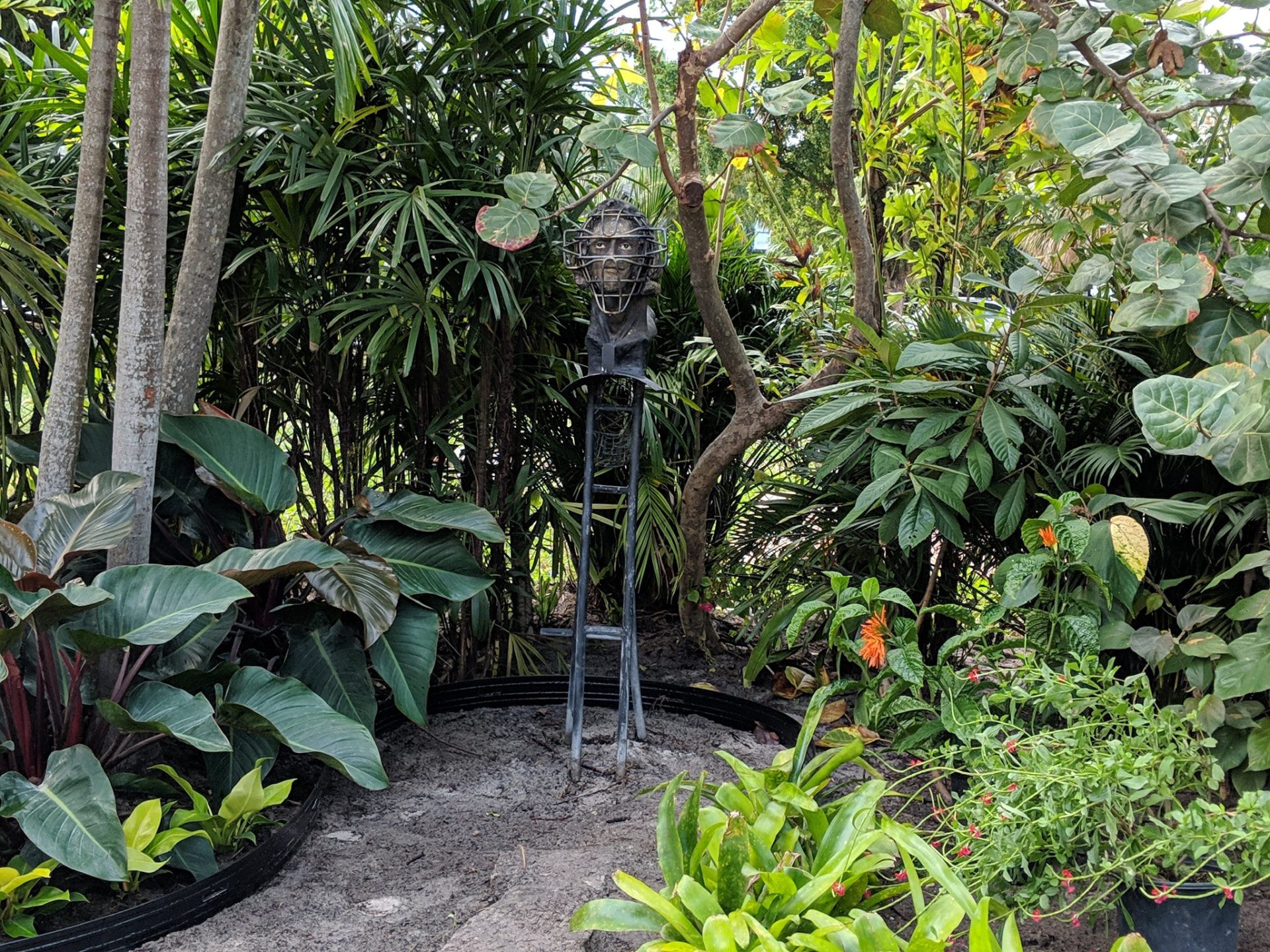 Layered tropical garden planting surrounding a tall metal figure sculpture