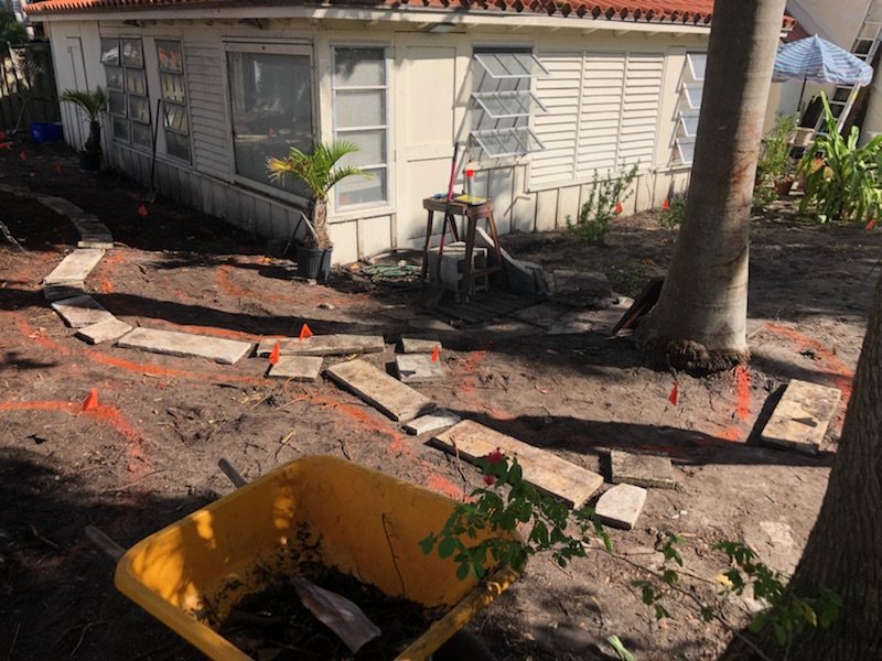 Curving garden layout marked in bare soil with flags and pavers during landscape preparation