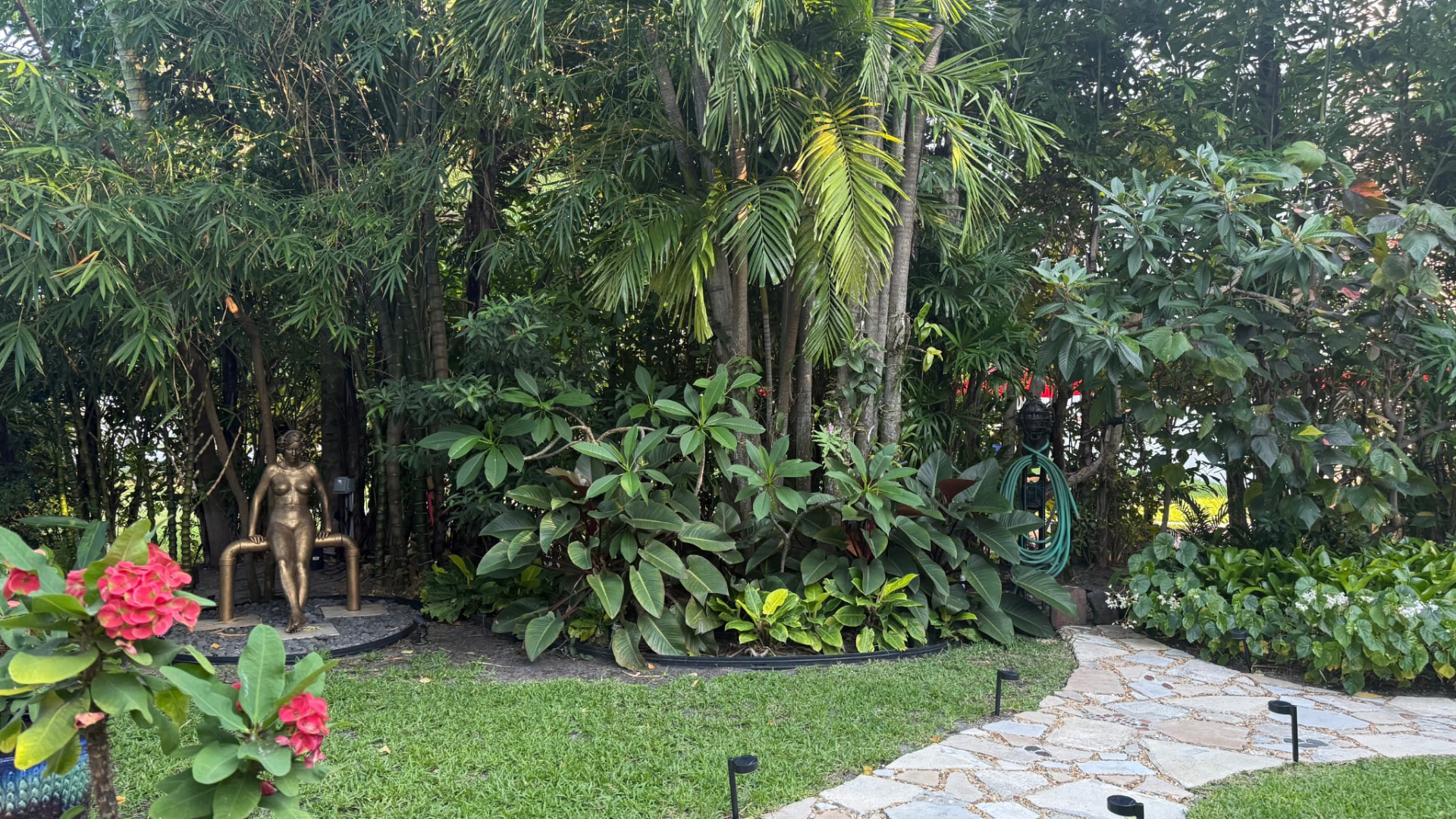 Tropical residential landscape with palms, flowering plants, lawn and a stone walkway in the Palm Beach area