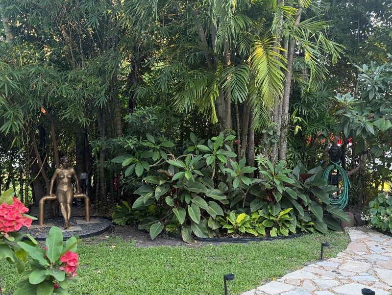 Layered tropical planting bed with a bronze statue and stone path at a Palm Beach property